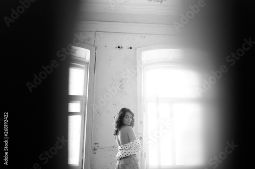 A young woman in a blouse exposes her back indoors. © Alexander