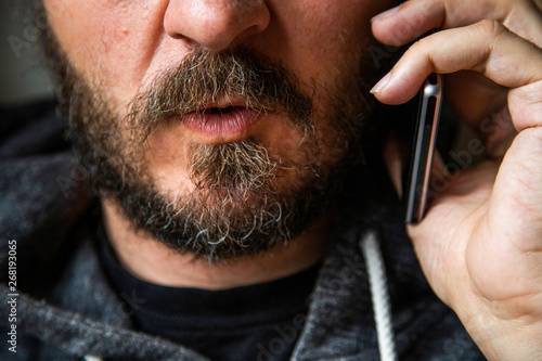 Close up portrait of bearded man talking on smart phone, focus on lips, no eyes, secret talk, criminal threating someone