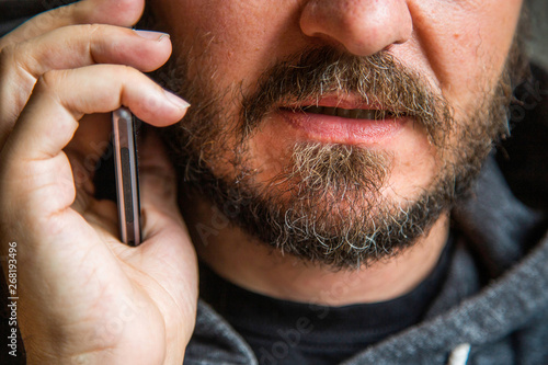 Close up portrait of bearded man talking on smart phone, focus on lips, no eyes, secret talk, criminal threating someone