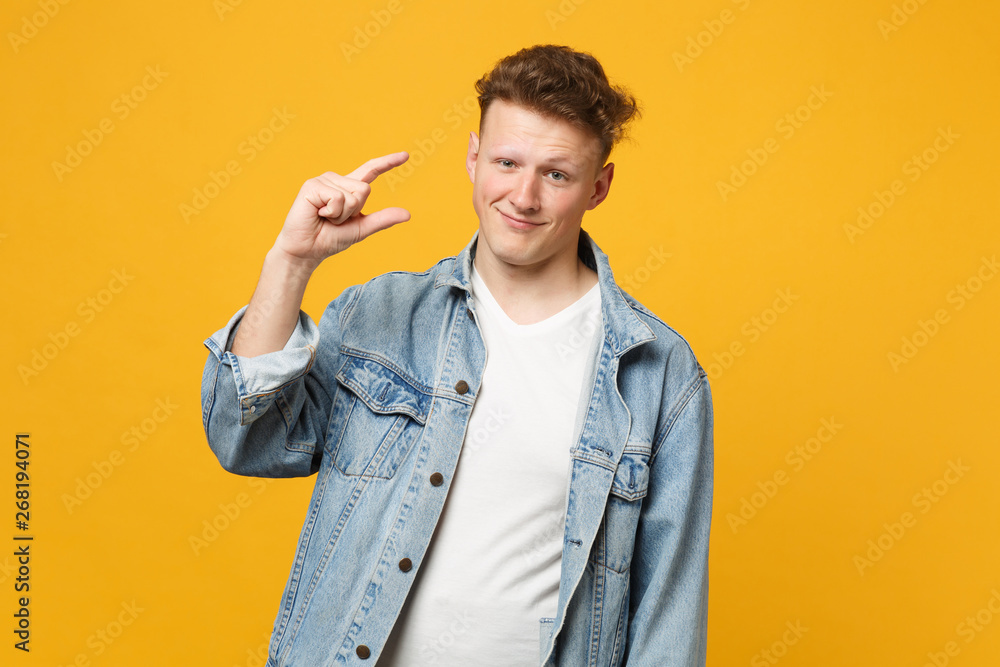 Portrait of smiling young man in denim casual clothes gesturing demonstrating size with workspace isolated on yellow orange background. People sincere emotions, lifestyle concept. Mock up copy space.