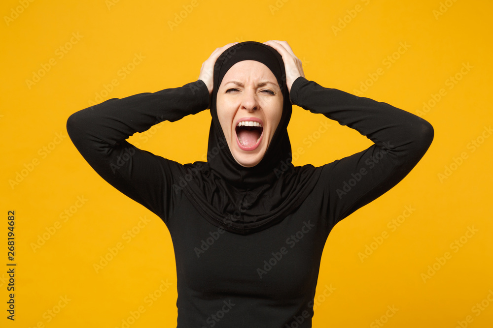 Sad upset crying confused young arabian muslim woman in hijab black clothes posing isolated on yellow wall background, studio portrait. People religious Islam lifestyle concept. Mock up copy space. Sad upset crying confused young arabian muslim woman in hijab black clothes posing isolated on yellow wall background, studio portrait. People religious Islam lifestyle concept. Mock up copy space.