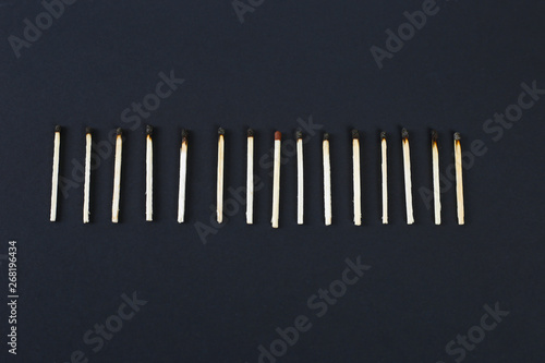 A row of burnt matches with new in centre on black background