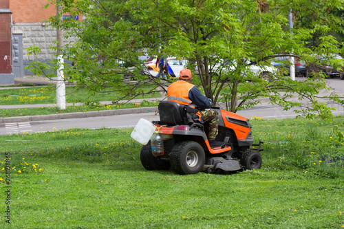 Worker municipal, city service, mows the grass on the lawn mower