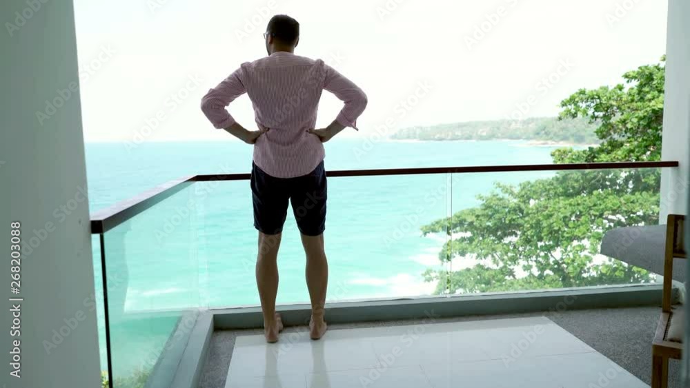 Young man walking out on terrace with sea view and stretching his arms, 4K Young man walking out on terrace with sea view and stretching his arms, 4K