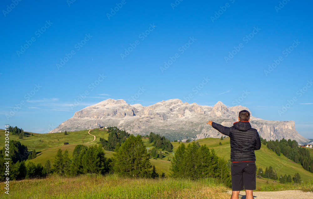 A person admires the fantastic Dolomites in Italy during the summer period. The massive Sella in the background. Hiker photographed from behind. Dolomites a Unesco World Heritage