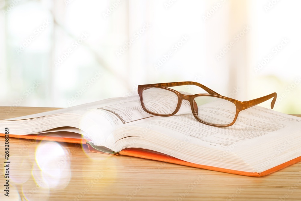 Close-up Black reading glasses and book on blurred library background Close-up Black reading glasses and book on blurred library background