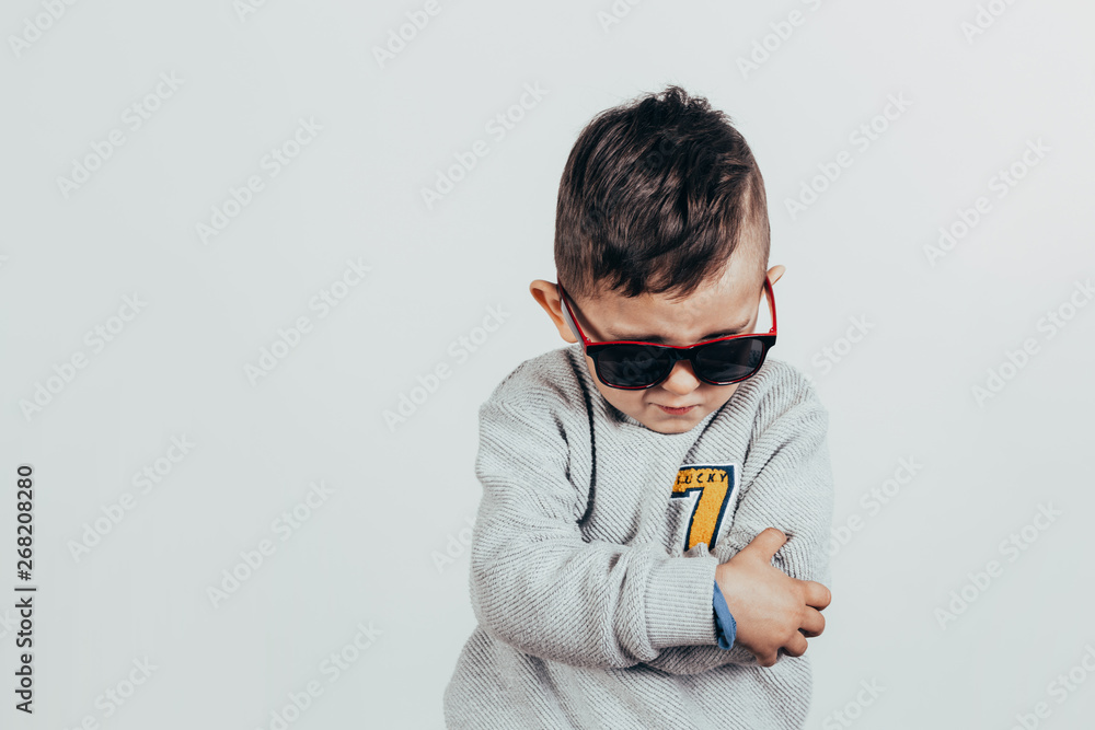 Photo of an adorable little boy wearing a sweater and sunglasses over a gray background. Vintage color. Human emotions Photo of an adorable little boy wearing a sweater and sunglasses over a gray background. Vintage color. Human emotions