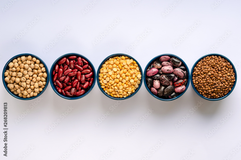 A variety of legumes. Lentils, chickpeas, peas and beans in blue bowls on a white background. Top view.