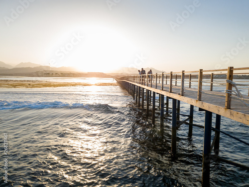 Beautiful landscape of long wooden pier and calm sea waves against sunset and mountains