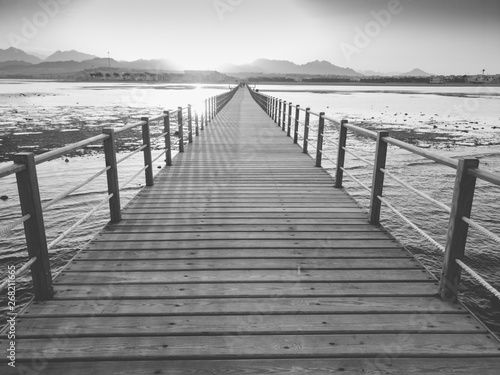 Black and white image of sun setting down over the ocean waves and long wooden pier