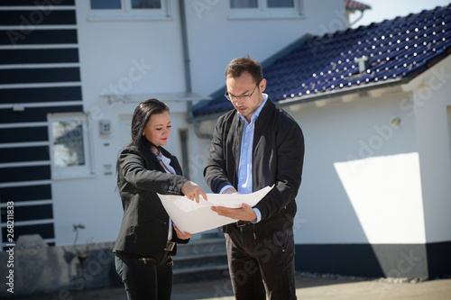 A real estate agent showing a customer house plan in front of the house