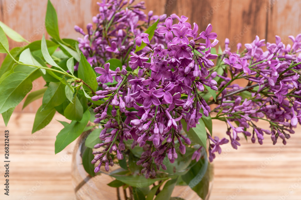 Fresh cut Purple Lilac Flowers in clear glass vase on wooden background. Syringa vulgaris. Fresh cut Purple Lilac Flowers in clear glass vase on wooden background. Syringa vulgaris.