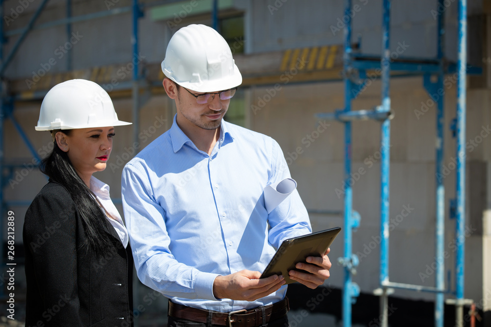 Two architects a man and a woman in construction in white helmets. Two architects a man and a woman in construction in white helmets.