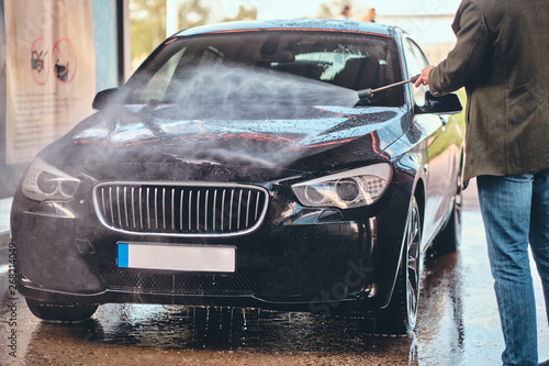 Busy man in jeans and blaser is washing his own car at car washing station. © Fxquadro