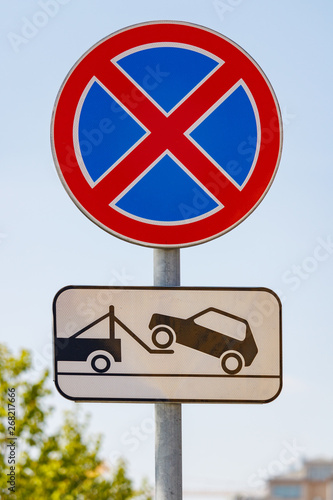Road sign prohibiting the stopping of the car with a tow truck signboard against blue sky in sunny day closeup