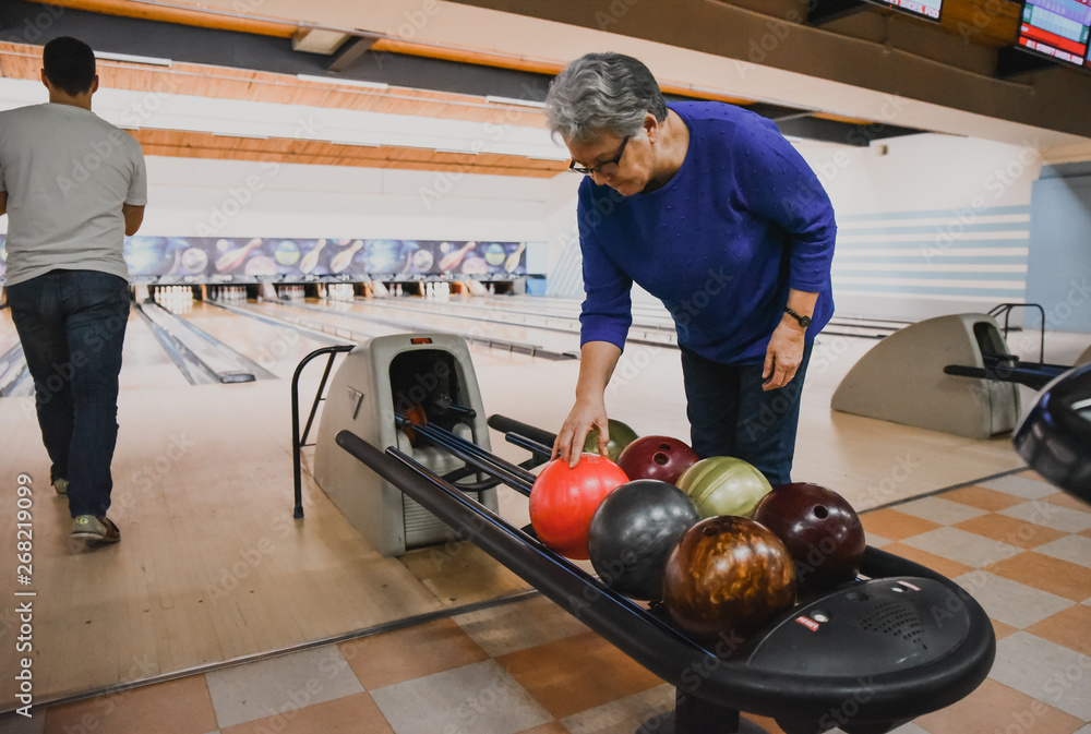 Older woman choosing bowling ball as man beside her bowls. 스톡 사진