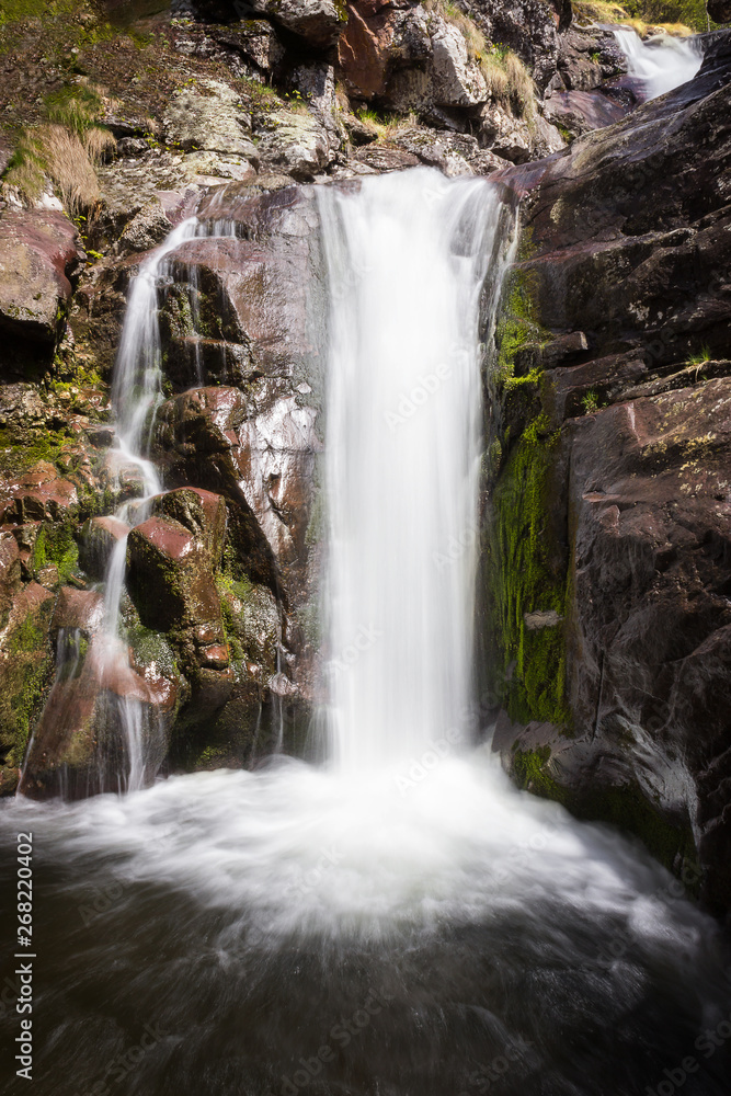 Obraz premium Unique, close up view of a scenic waterfall during spring streaming down the red, wet cliff with vibrant green moss
