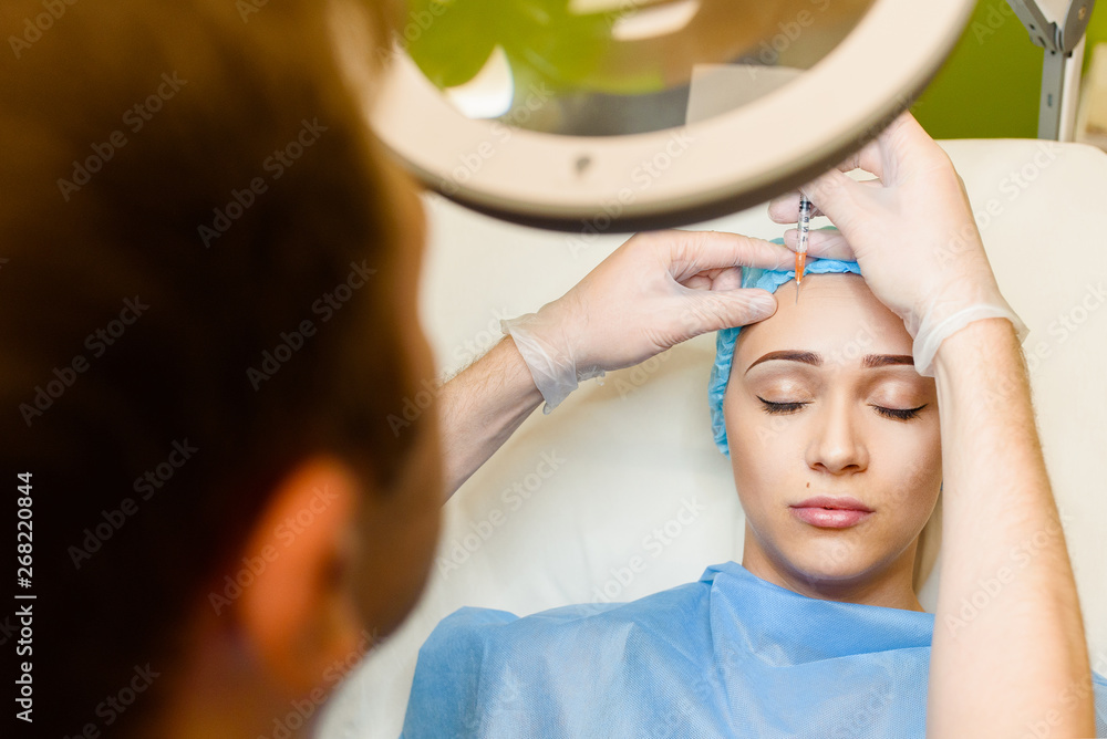 Naklejka premium Woman makes botox injections in forehead area. Doctor cleans the girl's face from wrinkles. Plastic surgery in private medical clinic.