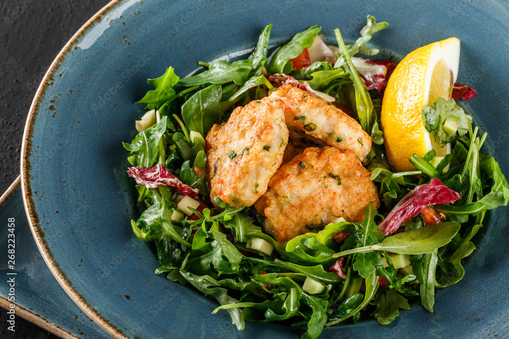Fresh salad with arugula, spinach, avocado and vegetable cutlets with herbs, garnished with lemon in plate over dark background. Healthy vegan food, clean eating, dieting, sports nutrition. Fresh salad with arugula, spinach, avocado and vegetable cutlets with herbs, garnished with lemon in plate over dark background. Healthy vegan food, clean eating, dieting, sports nutrition.