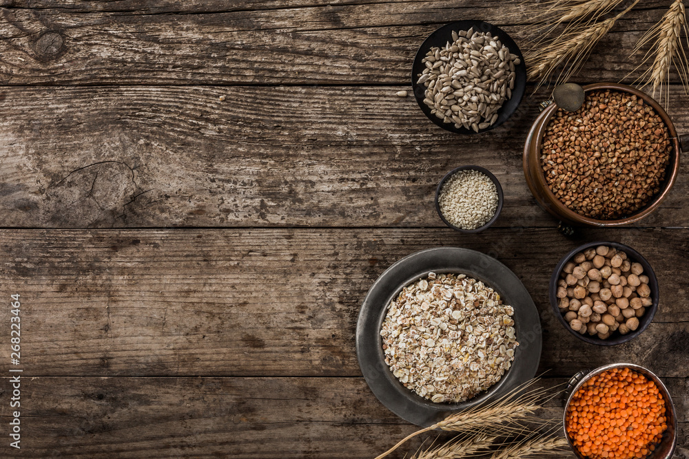 Superfoods and cereals selection in bowls, chickpeas, lentils, buckwheat, oatmeal, flax seeds, sunflower seeds on rustic wooden background. Healthy food concept, top view, flat lay, copy space