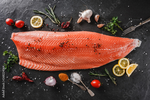 Fresh raw salmon fish steak with spices on dark stone background. Creative layout made of fish, top view, flat lay.