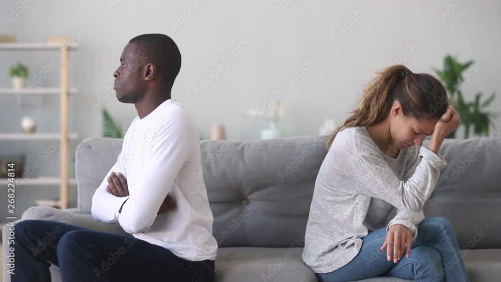 Unhappy stubborn mixed ethnicity young couple sit separately on sofa Unhappy stubborn mixed ethnicity young couple sit separately on sofa