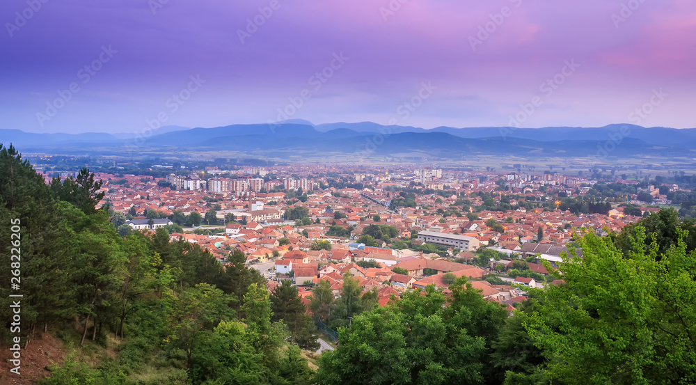 Blue hour sky over Pirot city and green foreground trees creating a natural frame around the cityscape