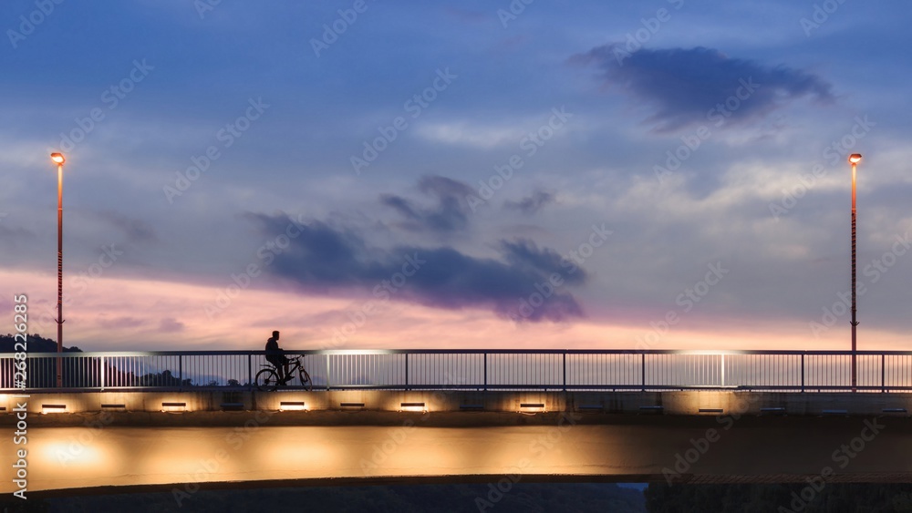 Silhouette of a boy on a bicycle on a bridge during colorful sunset Silhouette of a boy on a bicycle on a bridge during colorful sunset