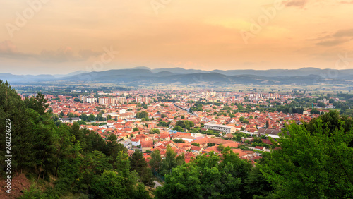Golden hour sky over sunlit Pirot city in Serbia and green foreground trees