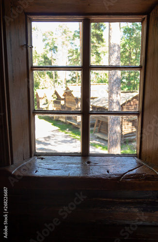 Old authentic 19th century wooden peasant house window with wooden window sill damaged by people and time  and a view of Seurasaari village in Helsinki in Finland on a summer day.
