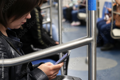 Young woman sits with smartphone in a train of a metro. Interior of subway car, train trip