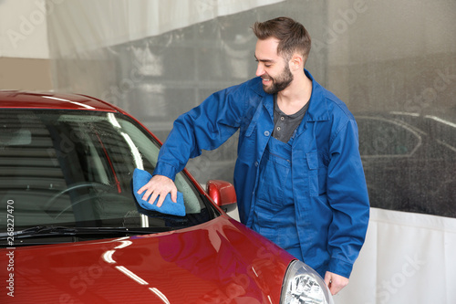 Worker cleaning automobile windshield with rag at car wash