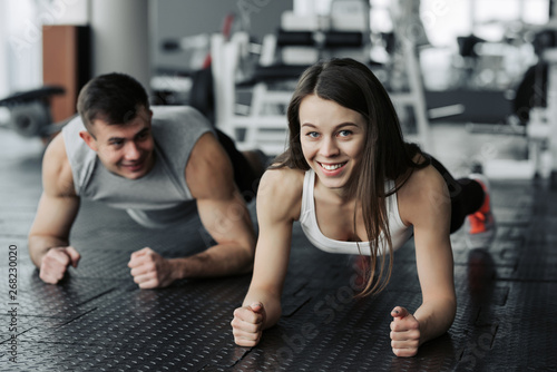 Young muscular couple doing doing hard workout at the gym. Doing plank in the gym.