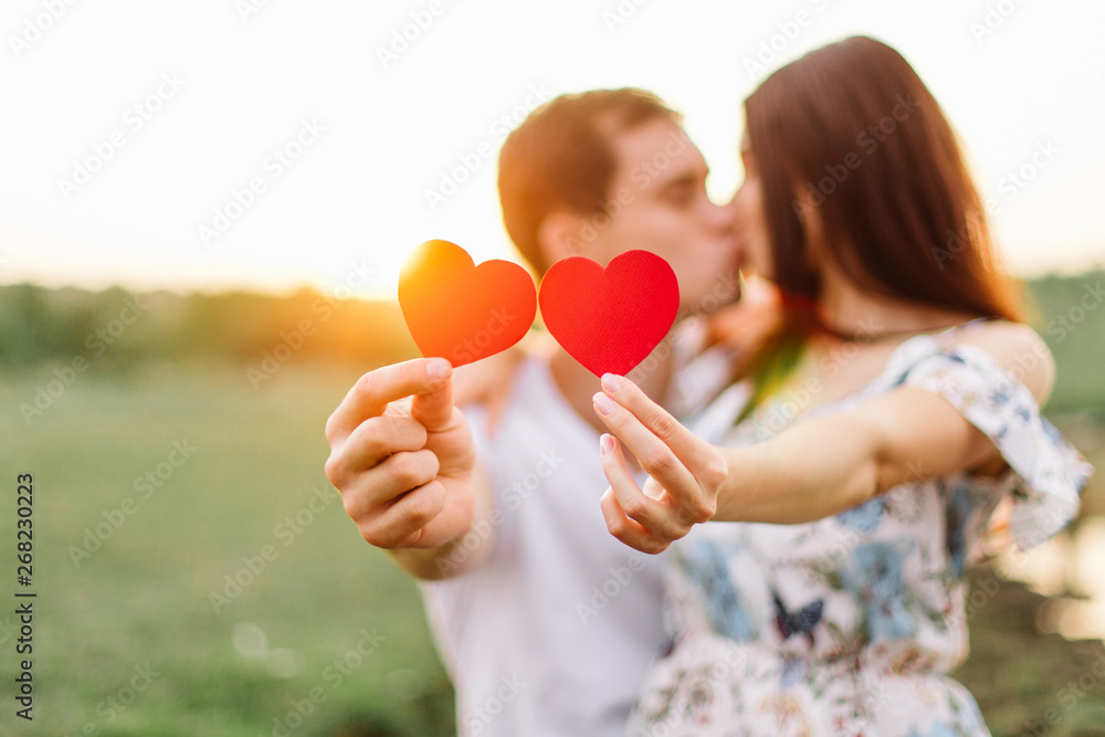 Young loving couple hugging near lake with red paper heart in hand. Young loving couple hugging near lake with red paper heart in hand.