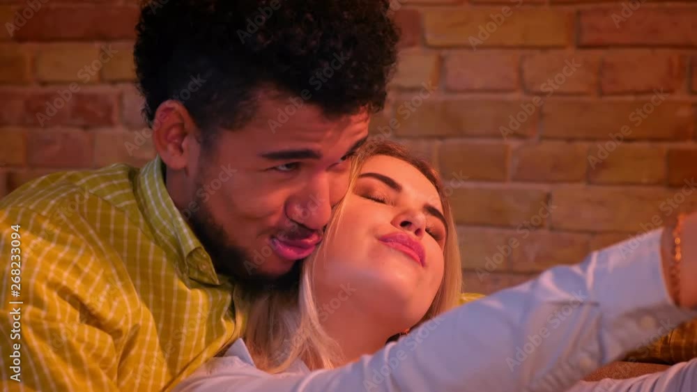 Close-up shot of african guy and caucasian girl shooting selfie-photos on phone making duck face joyfully. Close-up shot of african guy and caucasian girl shooting selfie-photos on phone making duck face joyfully.