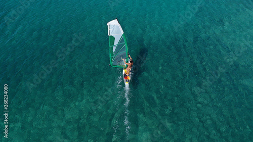 Aerial top view photo of fit man practising wind surfing in exotic open ocean bay with crystal clear emerald sea