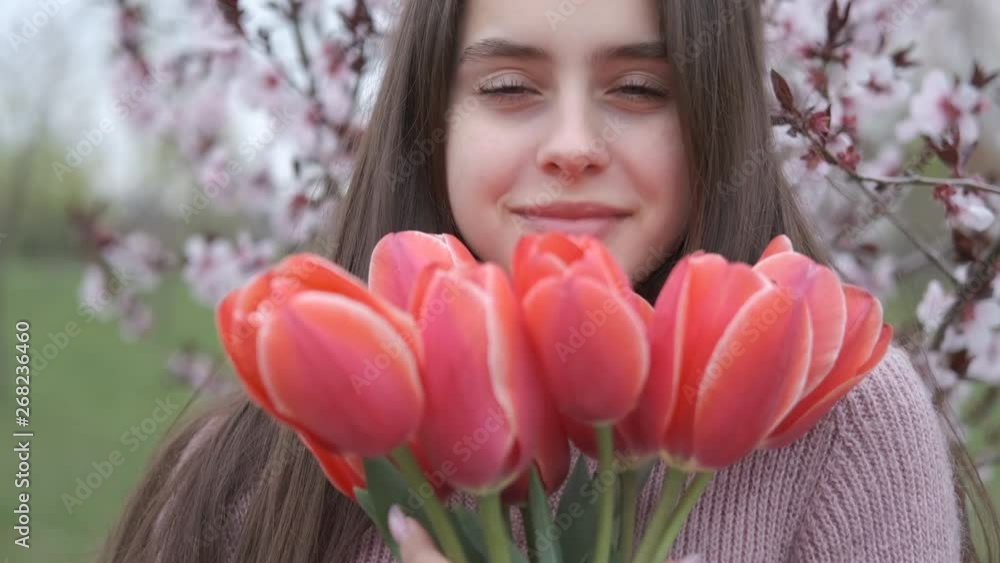 Portrait of a happy girl with tulips. Beautiful young girl with a bouquet of red tulips on a background of blooming sakura. Portrait of a happy girl with tulips. Beautiful young girl with a bouquet of red tulips on a background of blooming sakura.