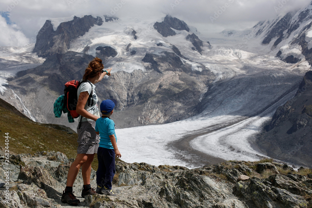 Sunnegga, Switzerland - August 15, 2018: Single parent family, mother and son, on their holidays at the edge of a mountain admiring an alpine glacier in Switzerland.