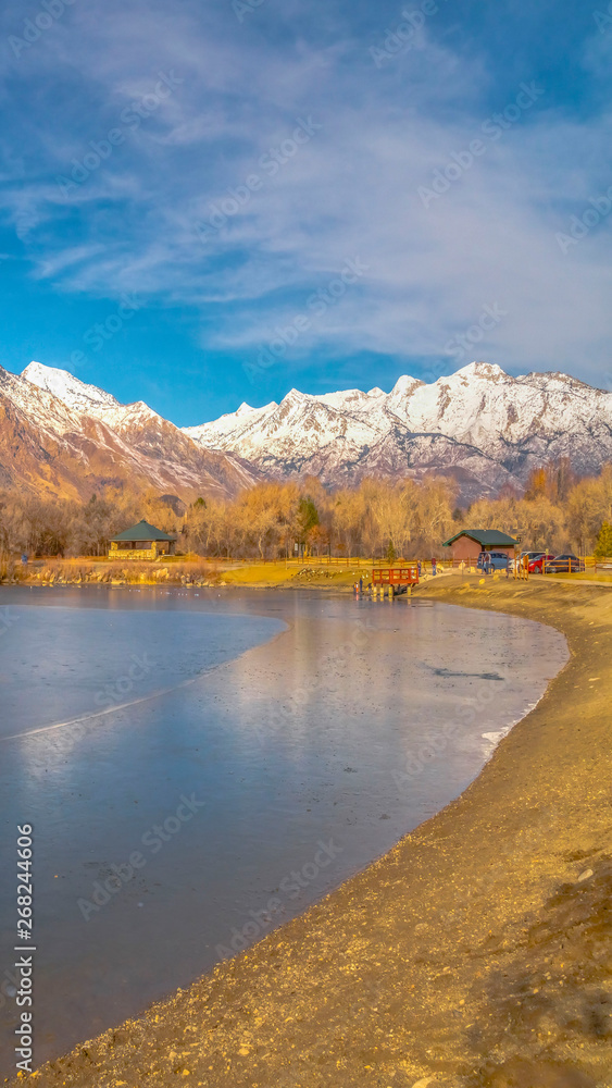 Vertical Scenic panorama of a lake against snow capped mountain and blue sky in winter