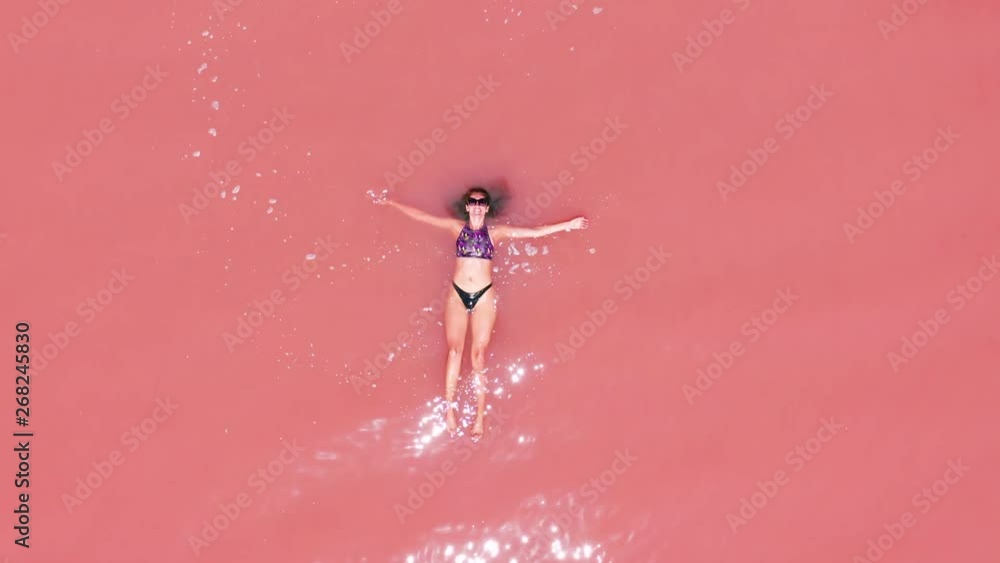 Aerial view of an attractive woman in a bikini floating in pink salt lake. Aerial view of an attractive woman in a bikini floating in pink salt lake.