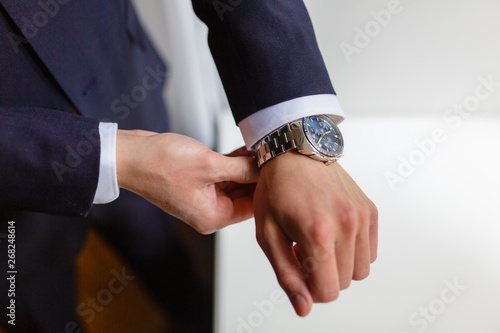 Closeup designer watch on businessman hand, he looks on the time and hurrying. A man in an expensive suit straightens the cuffs of his shirt.