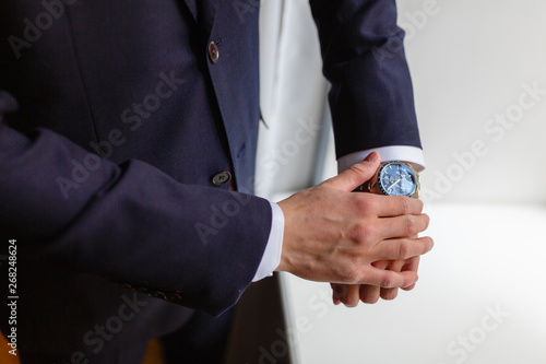 Closeup designer watch on businessman hand, he looks on the time and hurrying. A man in an expensive suit straightens the cuffs of his shirt.