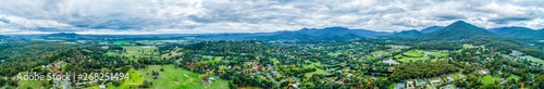 Ultra wide aerial panorama of scenic rural landscape with houses surrounded by trees, grasslands, and mountains. © Greg Brave