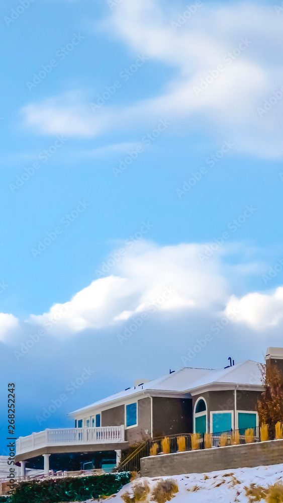 Vertical Homes on snowy hill against sky with puffy clouds