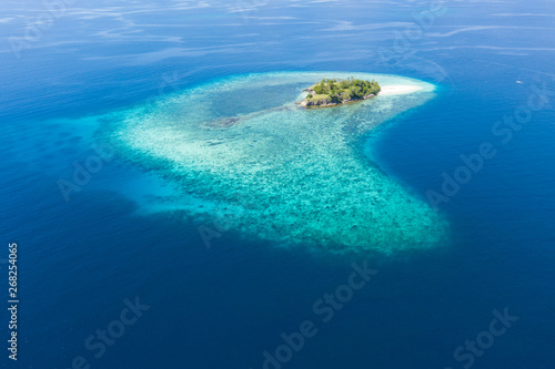 Seen from a bird's eye view, an idyllic island is surrounded by a healthy coral reef in Komodo National Park, Indonesia. This tropical area is known for its marine biodiversity as well as its dragons.