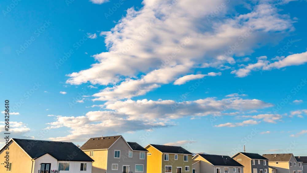Fototapeta premium Clear Panorama Row of houses under a vibrant blue sky with fluffy clouds on a sunny day