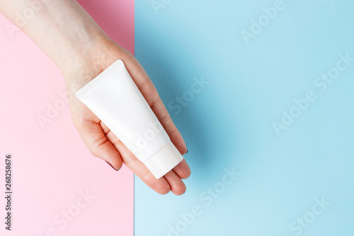 Tube with cream in female hand, blue and pink background, top view, cosmetics care concept