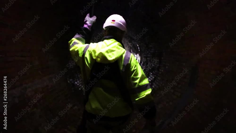 A sewer district worker leads the path with a light down an old 19th-century sewage tunnel. A sewer district worker leads the path with a light down an old 19th-century sewage tunnel.