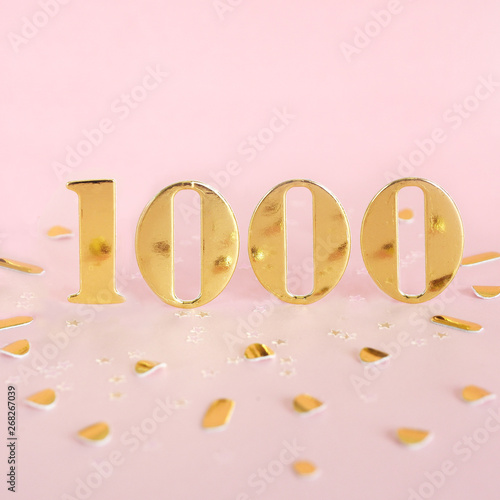 The number 1000 in golden numbers on a pink background and golden confetti. Space for text... photo