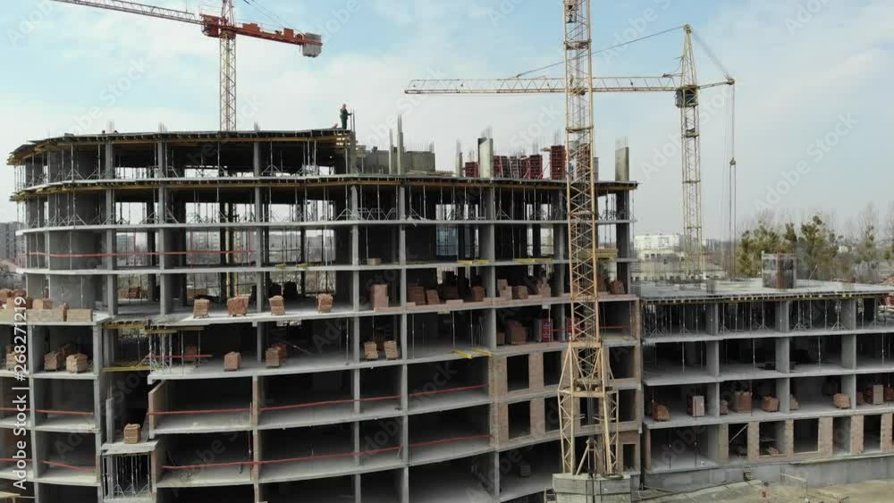 An aerial view of a residential building in construction. Tower cranes working by the building. 4K An aerial view of a residential building in construction. Tower cranes working by the building. 4K